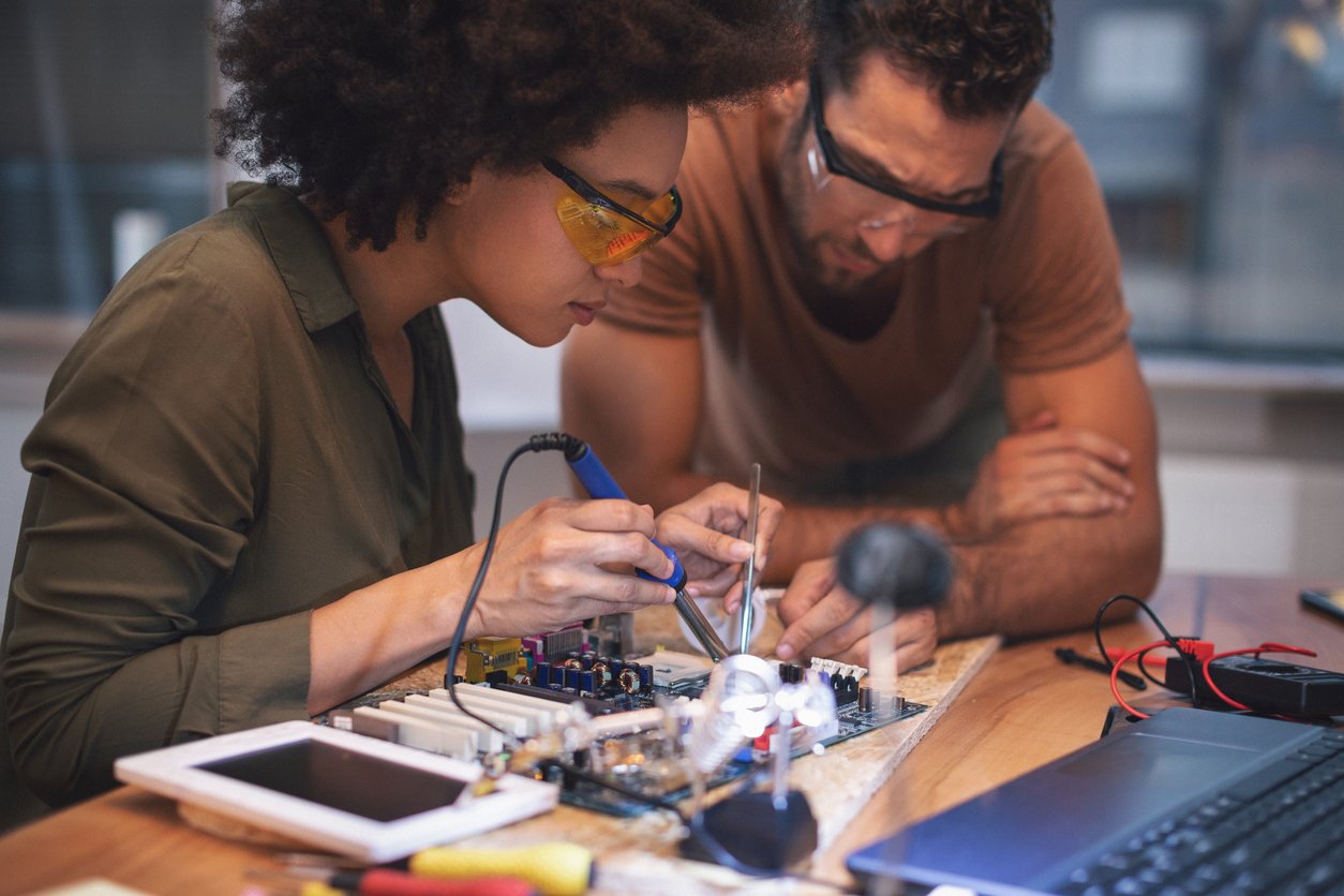 Two people working on soldering pieces to PCB. 7 Types of PCB Soldering Defects to Watch Out For